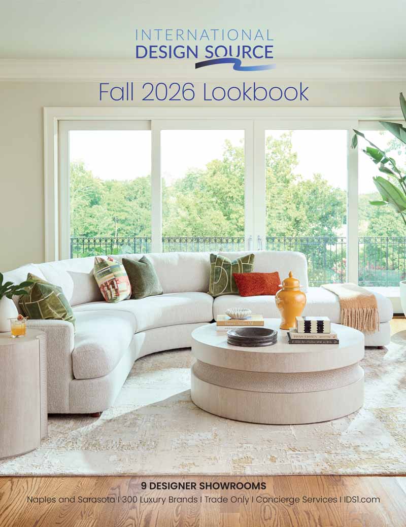 International Design Source Fall 2026 Lookbook cover featuring a curved cream sectional sofa with green and rust accent pillows, a round textured coffee table, and brass ginger jar accessories in a sunlit living room with floor-to-ceiling windows overlooking greenery. Text reads: 9 Designer Showrooms, Naples and Sarasota, 300 Luxury Brands, Trade Only, Concierge Services, IDS1.com.